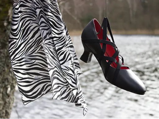 Black shoe with red straps beside zebra fabric